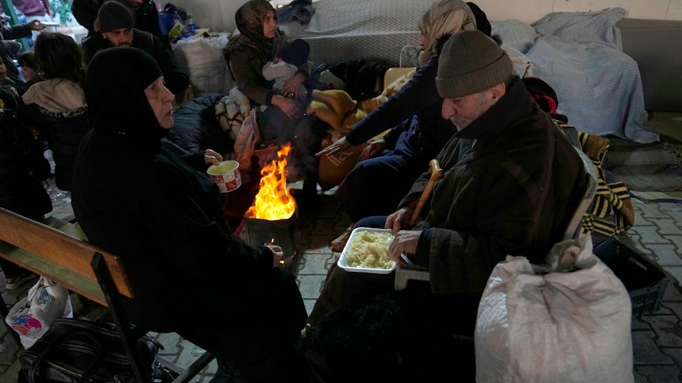 Menschen aus Syrien kauern um ein Feuer in einer Notunterkunft.