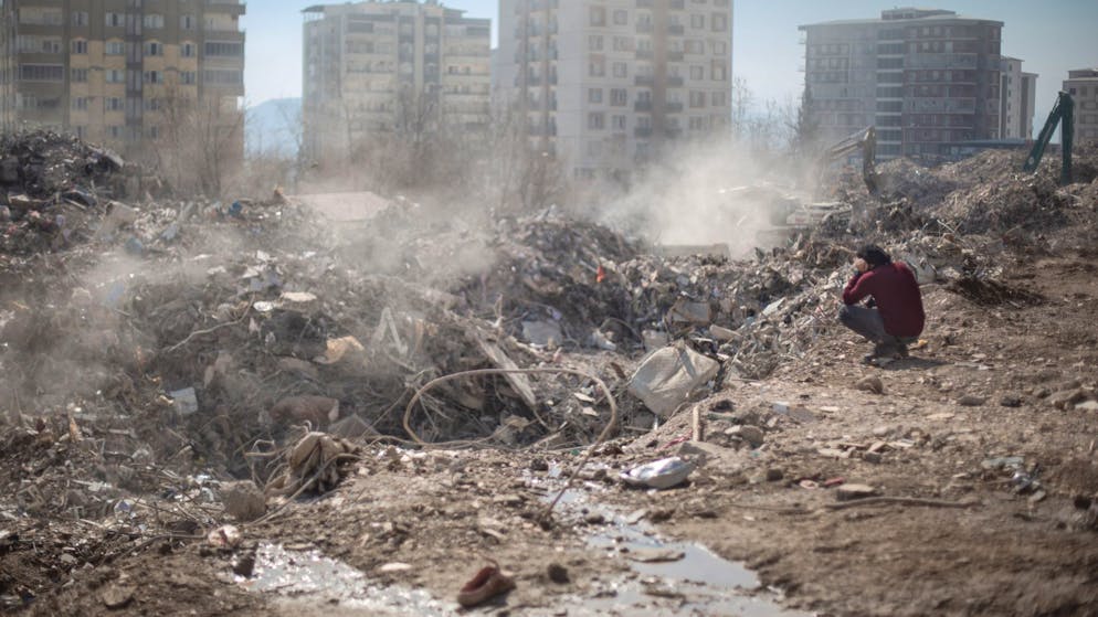 Mehr als 46.000 Tote – viele Schulen in Syrien zerstört - Gallery. Ein Mann sitzt neben seinem eingestürzten Haus in Kharamanmaras, während ein Suchteam unter den Trümmern weiter nach Menschen sucht.
