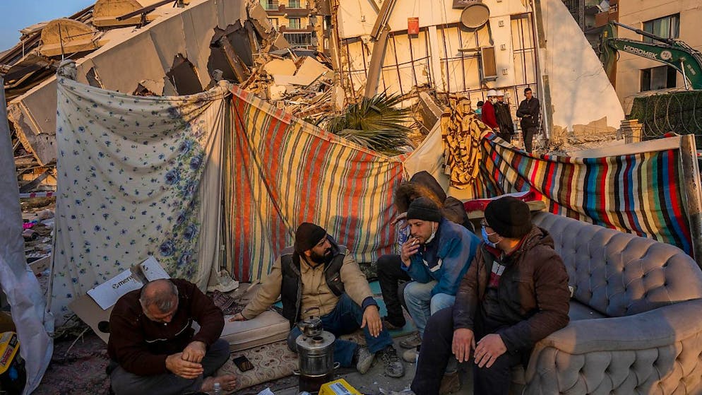 dpatopbilder - Männer sitzen vor den Trümmern bei dem Erdbeben zerstörter Gebäude. Die Zahl der Menschen, die in der Türkei durch das Erdbeben getötet worden sind, ist auf 41 020 gestiegen. Foto: Bernat Armangue/AP/dpa