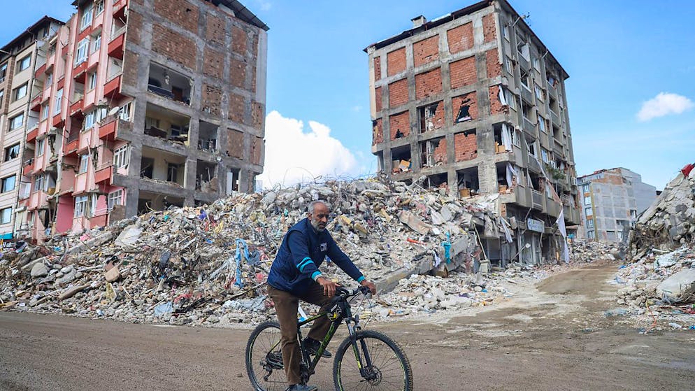 Ein Mann fährt mit dem Fahrrad an zerstörten Gebäuden entlang. Nach dem verheerenden Erdbeben am 06.02.2023 in der türkisch-syrischen Grenzregion kommt es immer wieder zu heftigen Nachbeben. Foto: Unal Cam/AP/dpa