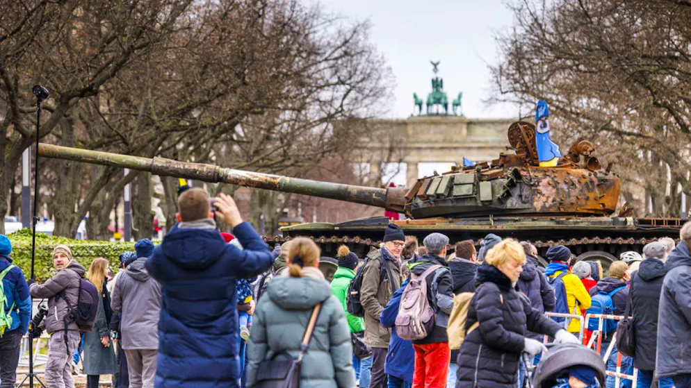 Passanten und Medienvertreter stehen vor einem in der Ukraine zerstörten russischen Panzer. Das Wrack steht auf einem Hänger vor der Botschaft Russlands in Berlin.