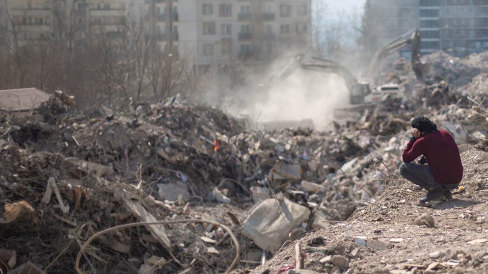 Blick ins Leere: Ein Mann neben seinem eingestürzten Haus, während ein Bagger Trümmer wegschafft.
