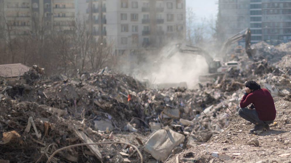 PRODUKTION - Ein Mann sitzt neben seinem eingestürzten Haus, während ein Suchteam unter den Trümmern im Epizentrum des Erdbebens nach Menschen sucht. Foto: Ahmed Deeb/dpa