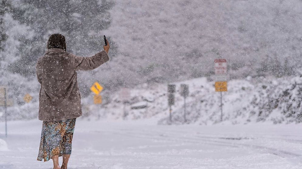 dpatopbilder - Eine Frau steht auf einer schneebedeckten Straße und macht ein Selfie im Angeles National Forest in der Nähe von La Canada Flintridge. Foto: Jae C. Hong/AP/dpa