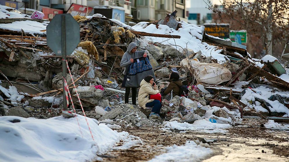Menschen sitzen zwischen den Trümmern vor einem eingestürzten Gebäude im türkischen Malatya. Foto: Emrah Gurel/AP/dpa