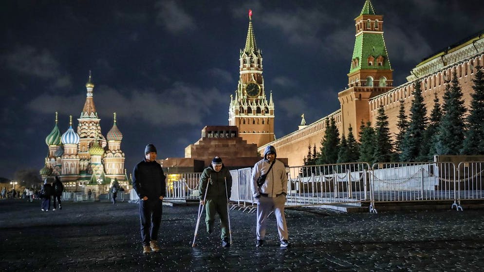 Passanten am 25. März 2023 vor dem hell erleuchteten Kreml in Moskau. 