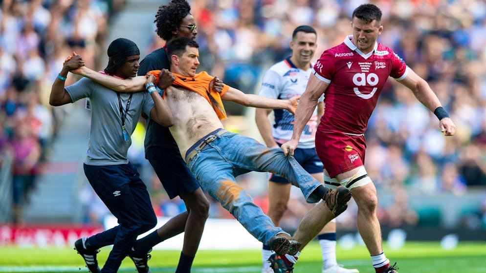 Un attivista di Just Stop Oil portato fuori campo da membri della sicurezza e giocatori durante la partita di rugby tra i Sharks e i Saracens.