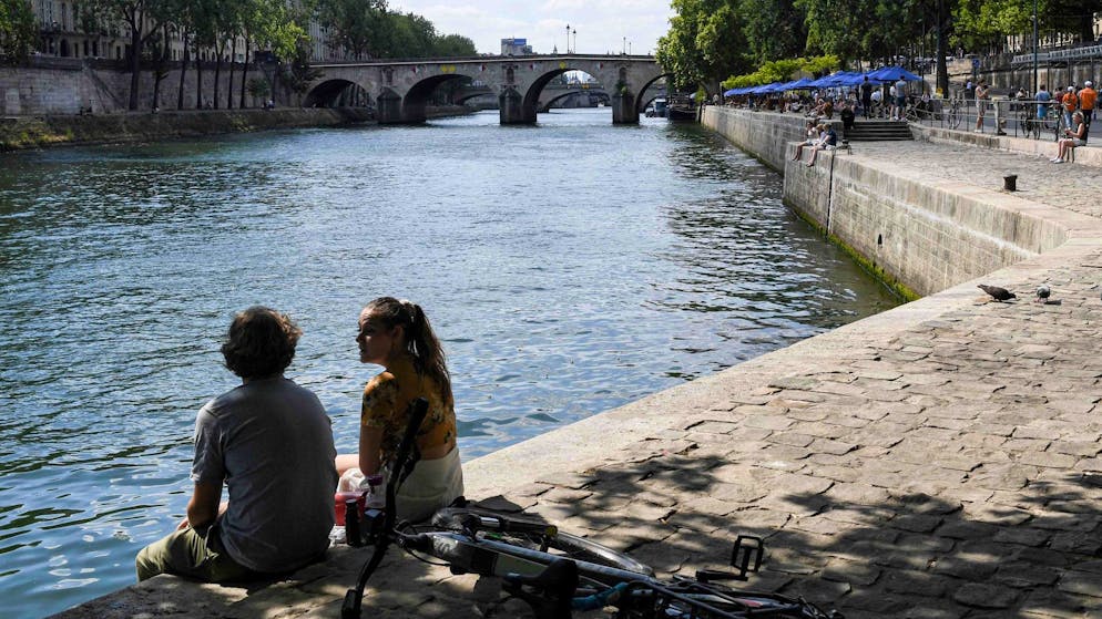 Zwei junge Leute sitzen am Ufer der Seine in Paris.
