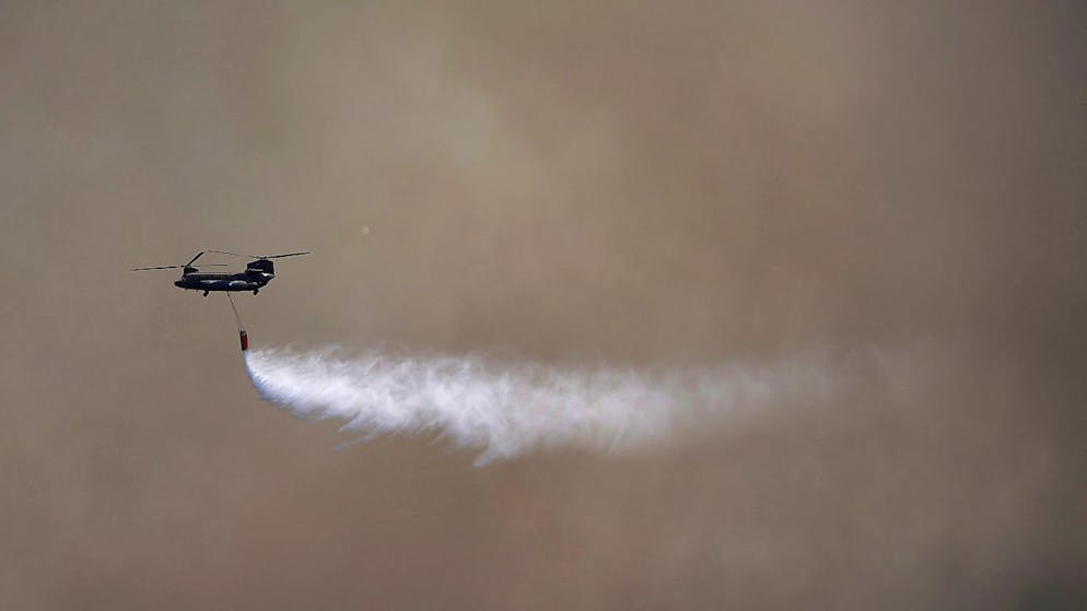 Ein Militärhubschrauber wirft Wasser auf ein Feuer auf ein Brandgebiet. Foto: Thanassis Stavrakis/AP/dpa