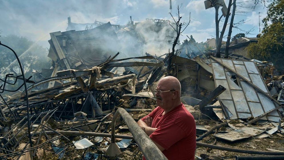 Eine Mann sieht zu, wie Rettungskräfte nach einem Angriff auf die südukrainische Region Odessa an einem zerstörten Gebäude arbeiten. Foto: Libkos/AP/dpa
