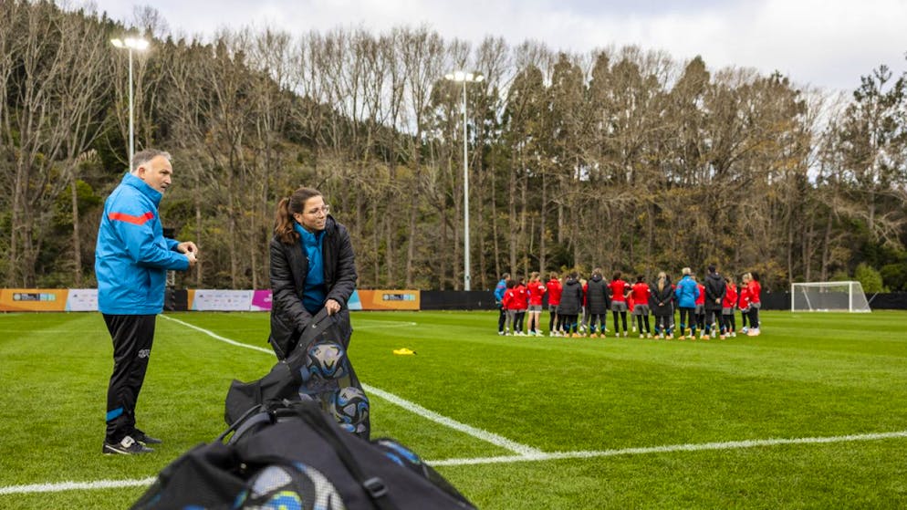 Vier Personen im Hintergrund des Schweizer Nationalteams - Gallery. Materialwartin Martina Pfluger, in der Mitte, legt im Training in Dunedin dem Nationalteam die Bälle bereit.