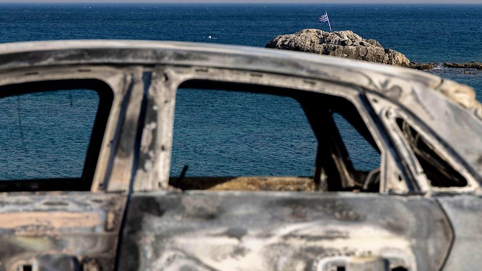 Ein verbranntes Fahrzeug steht am Strand auf der Insel Rhodos. Auch in Mittelgriechenland sind zahlreiche Brände ausgebrochen. Foto: Christoph Reichwein/dpa