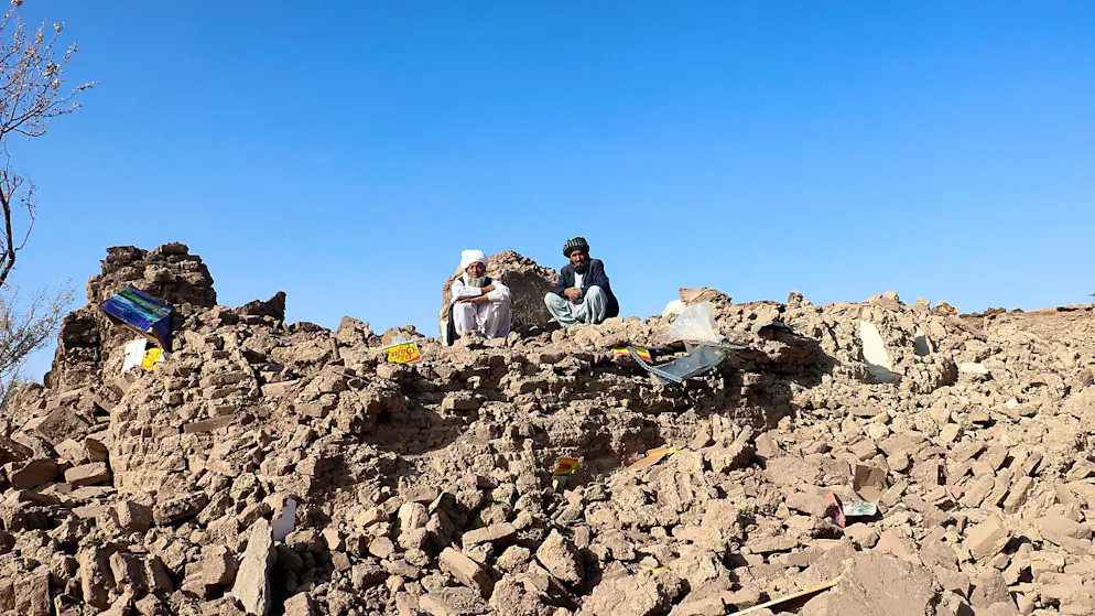 Afghanische Männer sitzen auf den Trümmern ihrer zerstörten Häuser nach einem Erdbeben in der Provinz Herat. Foto: Omid Haqjoo/AP/dpa