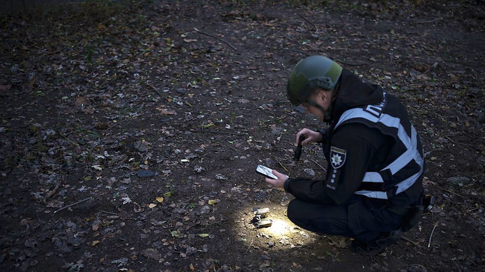 Officier de police ukrainien à la recherche de débris de drone samedi près du site d'une explosion consécutive à une vague de ces engins militaires volants en provenance de la Russie.