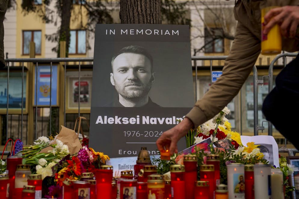 Una donna posa una candela accesa accanto a un poster del leader dell'opposizione russa Alexei Navalny, fuori dall'ambasciata russa a Bucarest, in Romania, domenica 18 febbraio 2024.