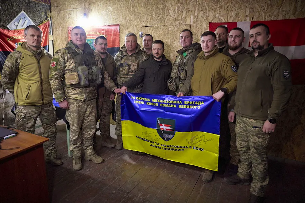 Il Presidente dell'Ucraina Volodymyr Zelensky (C) con i militari dopo aver firmato una bandiera durante la sua visita al posto di comando del battaglione della 14ª brigata meccanizzata separata intitolata al principe Romano il Grande, vicino alla linea del fronte nella zona di Kupyansk, in Ucraina, il 19 febbraio 2024, durante l'invasione russa.