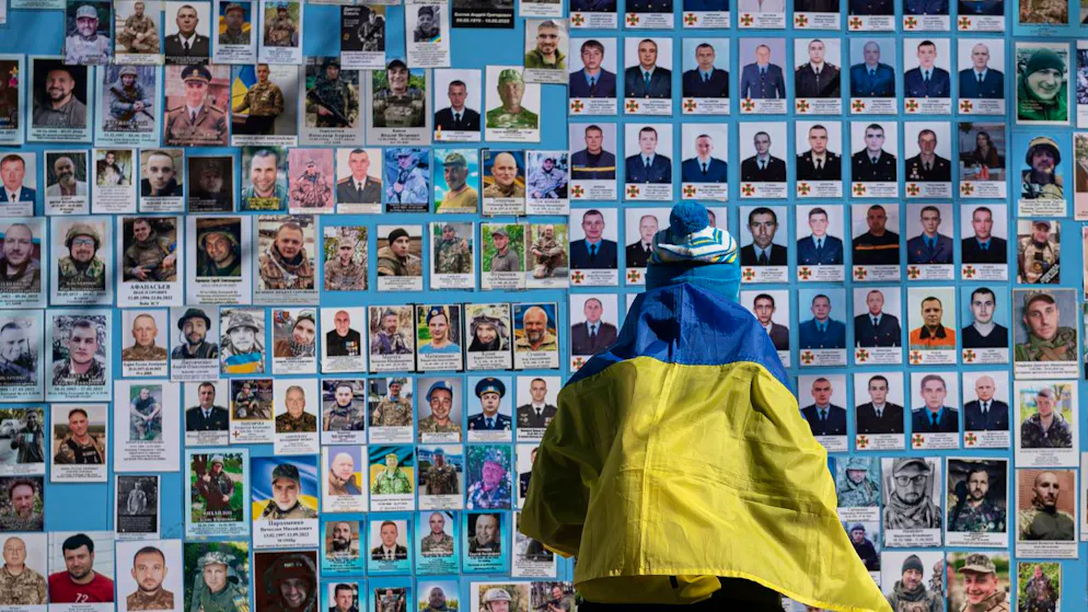 ARCHIV - Eine in eine ukrainische Flagge gehüllte Frau steht neben der Gedenkmauer für die gefallenen Soldaten der Ukraine im russisch-ukrainischen Krieg am ukrainischen Freiwilligentag. Foto: Andrew Kravchenko/AP/dpa
