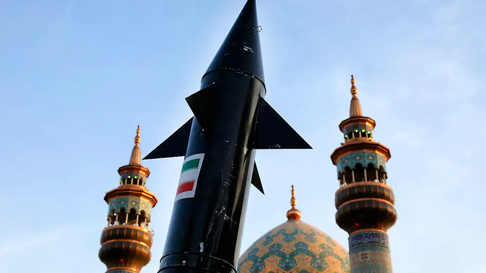 Ein Modell einer Rakete wird bei einer anti-israelischen Versammlung auf dem Felestin (Palästina) Platz von iranischen Demonstranten getragen, während im Hintergrund Minarette und die Kuppel einer Moschee zu sehen sind. Foto: Vahid Salemi/AP/dpa