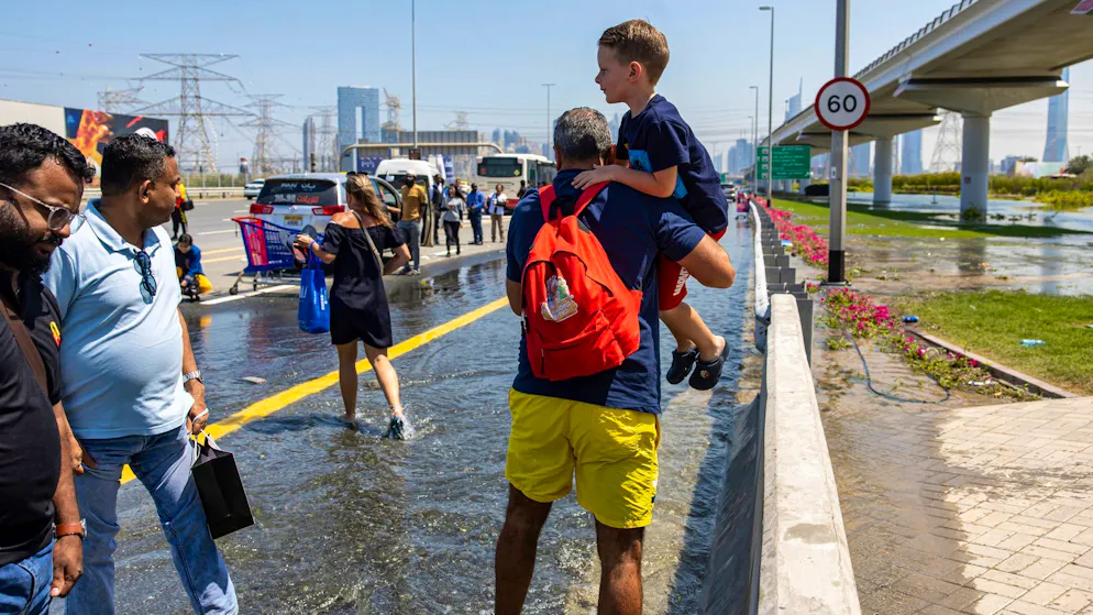 Ein Mann trägt ein Kind durch das von starkem Regen verursachte Hochwasser in Dubai.