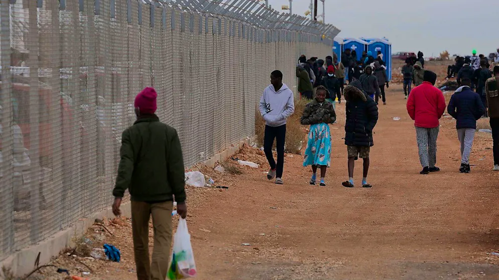 ARCHIV - Personen gehen am Zaun eines Aufnahmezentrums für Migranten in Zypern vorbei. Foto: Petros Karadjias/AP/dpa