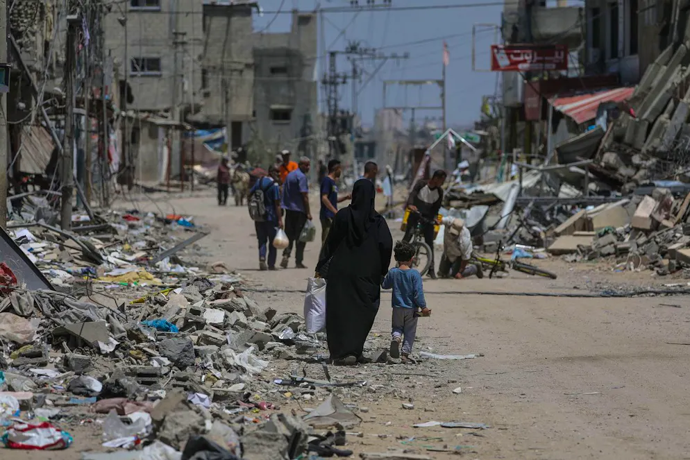 Palestinesi camminano tra case distrutte nel nord del campo profughi di Al Nusairat, nel sud della Striscia di Gaza, 29 aprile 2024.
