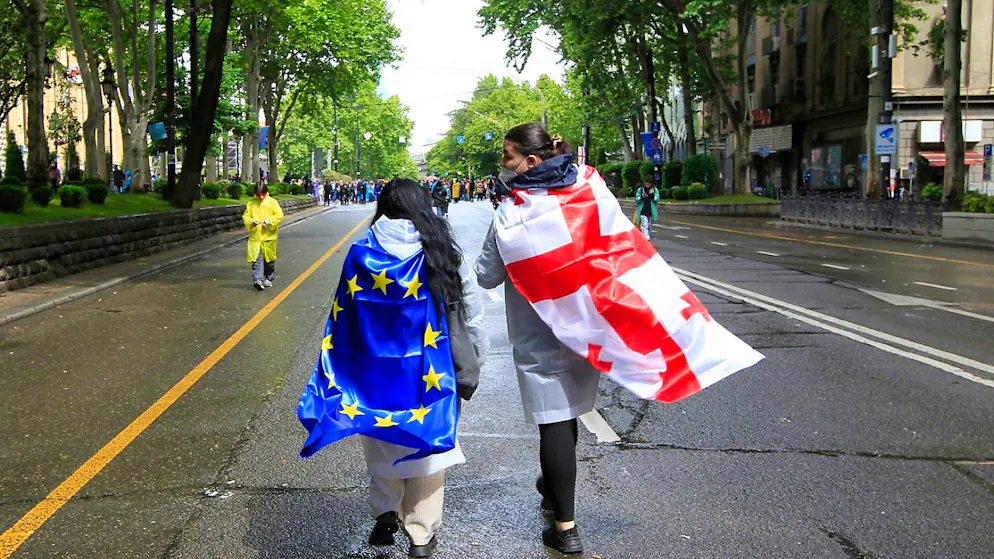 Zwei Demonstranten mit georgischer National- und EU-Flagge gehen während eines Protestes der Opposition gegen das «russische Gesetz» im Zentrum von Tiflis auf das Parlamentsgebäude zu. Foto: Shakh Aivazov/AP/dpa