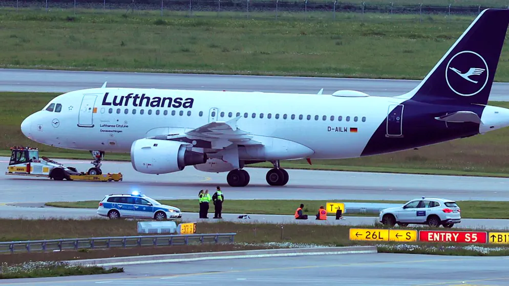Zwei Aktivisten haben sich auf einer Zufahrt für Start- und Landebahnen am Flughafen Franz-Josef-Strauß festgeklebt. Foto: Karl-Josef Hildenbrand/dpa