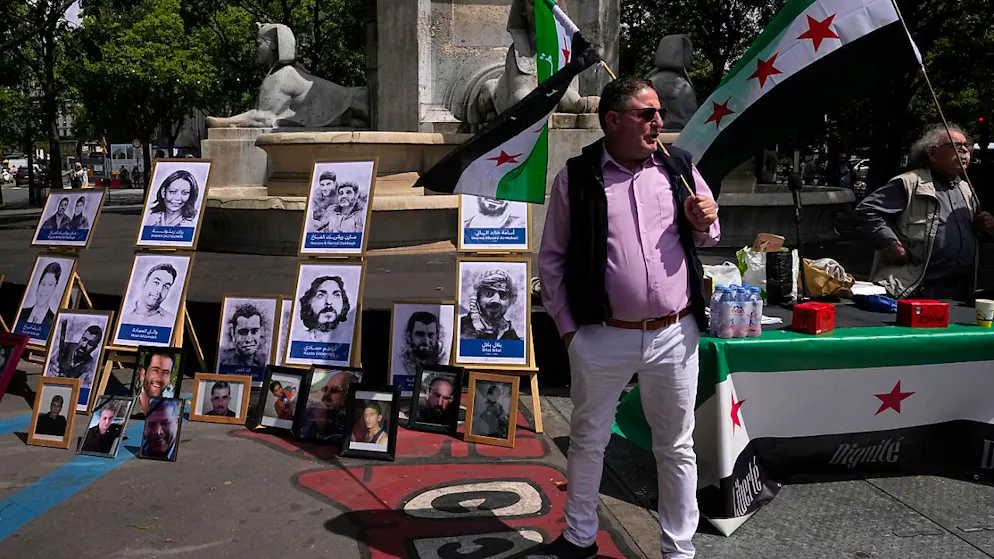 Aktivisten halten syrische Flaggen neben Porträts von mutmaßlichen Opfern des syrischen Regimes während einer Demonstration vor einem Gerichtssaal in Paris. Dort hat der Prozess gegen drei ranghohe syrische Beamte begonnen, die für den Tod von zwei französischen Staatsbürgern in Syrien verantwortlich sein sollen. Foto: Michel Euler/AP/dpa