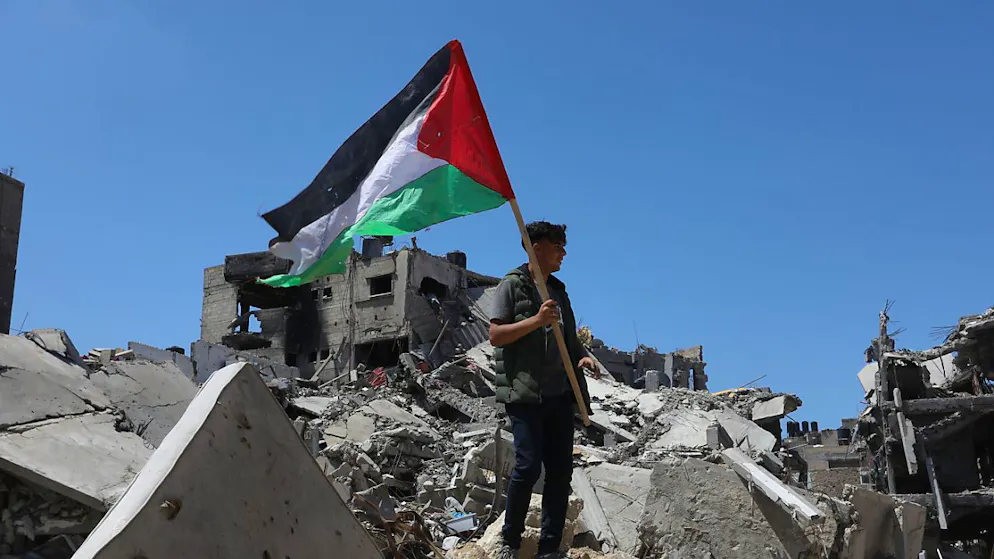 ARCHIV - Ein Palästinenser hält die palästinensische Fahne in der Hand, während er auf Trümmern nach israelischem Beschuss in Chan Junis steht. Norwegen, Irland und Spanien werden Palästina als Staat anerkennen. Das teilten der norwegische Ministerpräsident Støre, Irlands Premierminister Harris und der spanische Ministerpräsident Sánchez mit. Foto: Abed Rahim Khatib/dpa