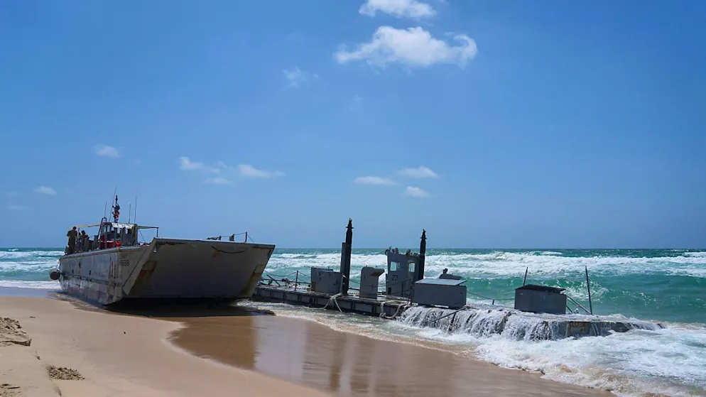 Ein angeschwemmtes Schiff der US-Armee und ein Stück der Anlegestelle sind am Strand zu sehen. Hohe Wellen und stürmische See haben die vor einer Woche errichtete provisorische Anlegestelle für humanitäre Lieferungen in den Gazastreifen beschädigt. Foto: Tsafrir Abayov/AP/dpa