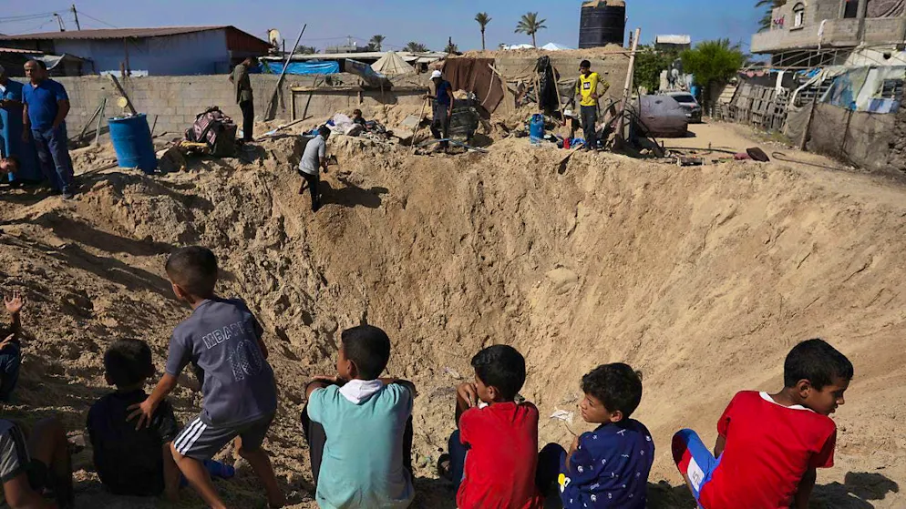 Palestinian children sit on the edge of a crater after an Israeli airstrike. Photo: Jehad Alshrafi/AP/dpa