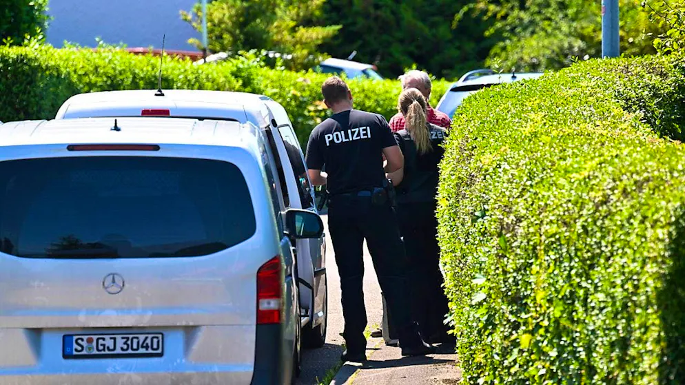Police officers and police vehicles stand in front of a crime scene where three people died in an act of violence the day before. Photo: Bernd Weißbrod/dpa