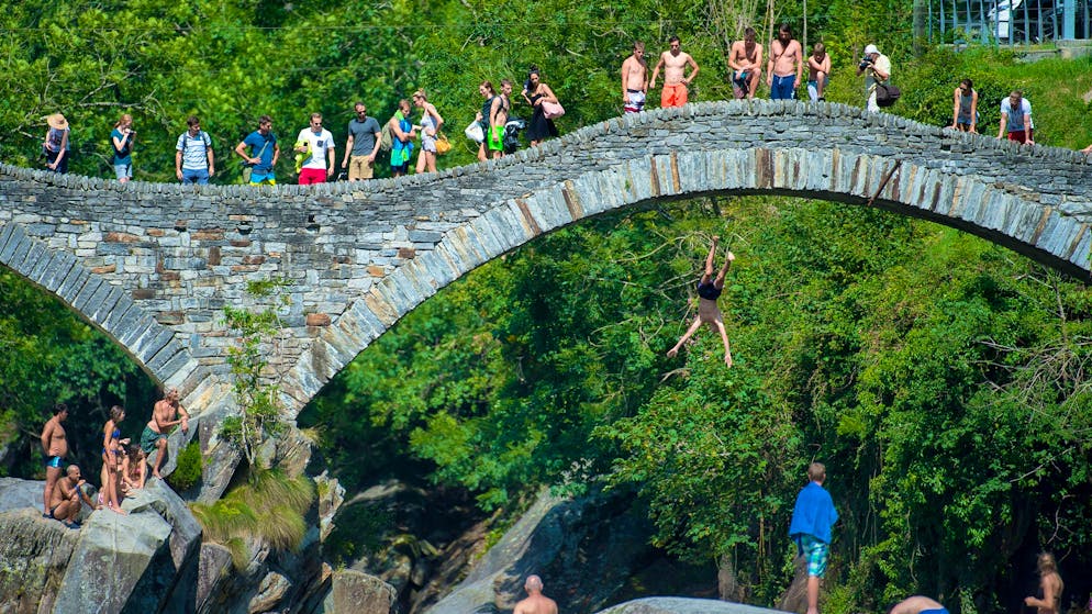Tourists enjoy the summer weather in the Verzasca near Lavertezzo TI, in the picture the historic bridge of Lavertezzo.