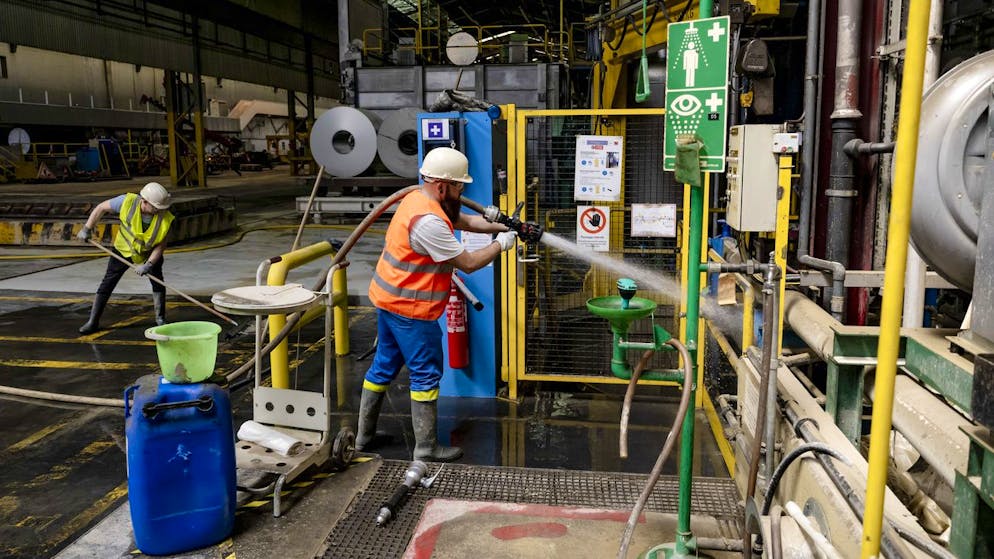 Zwei Mitarbeiter von Novelis reinigen den Schlamm zwischen den Maschinen auf dem Gelände in Siders (Bild vom 11. Juli).