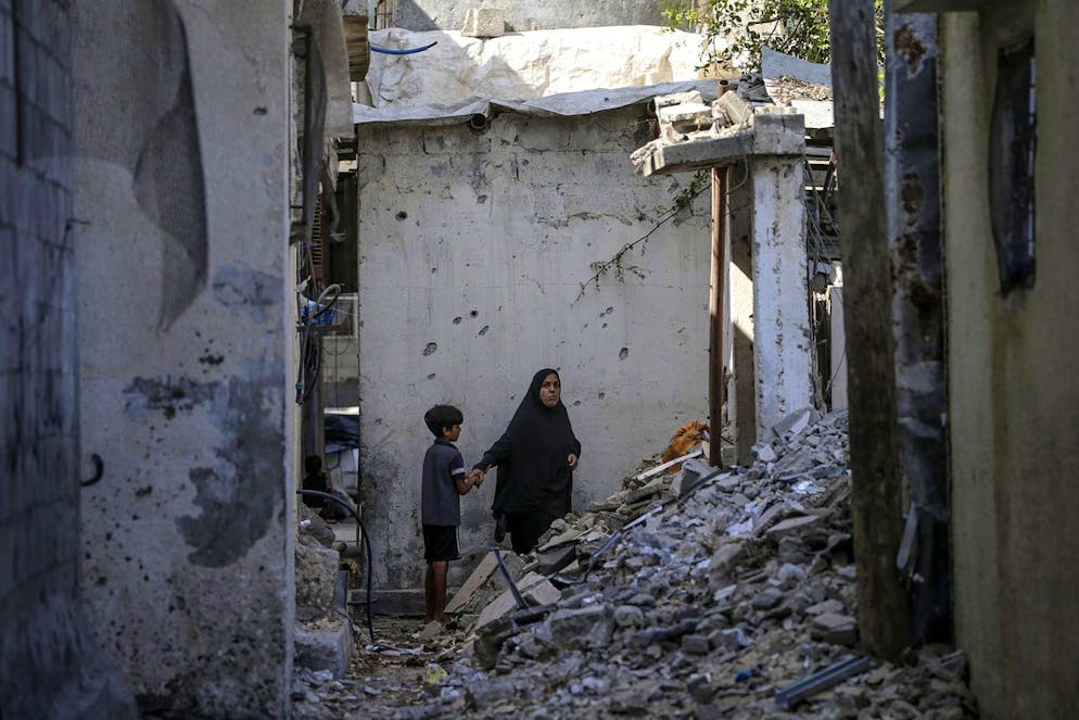 Una donna palestinese e suo figlio camminano accanto a una casa distrutta dopo un attacco aereo israeliano nel campo profughi di Al Maghazi, nella Striscia di Gaza, 14 agosto 2024 (immagine illustrativa).