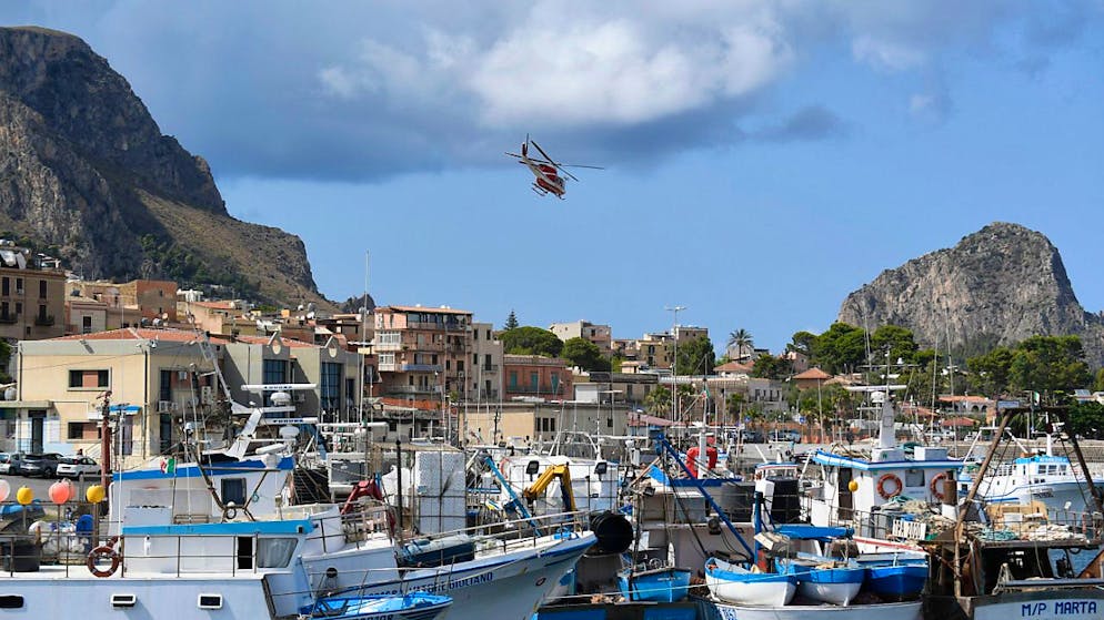 Ein italienischer Feuerwehrhubschrauber fliegt über den Hafen von Porticello. Foto: Salvatore Cavalli/AP/dpa