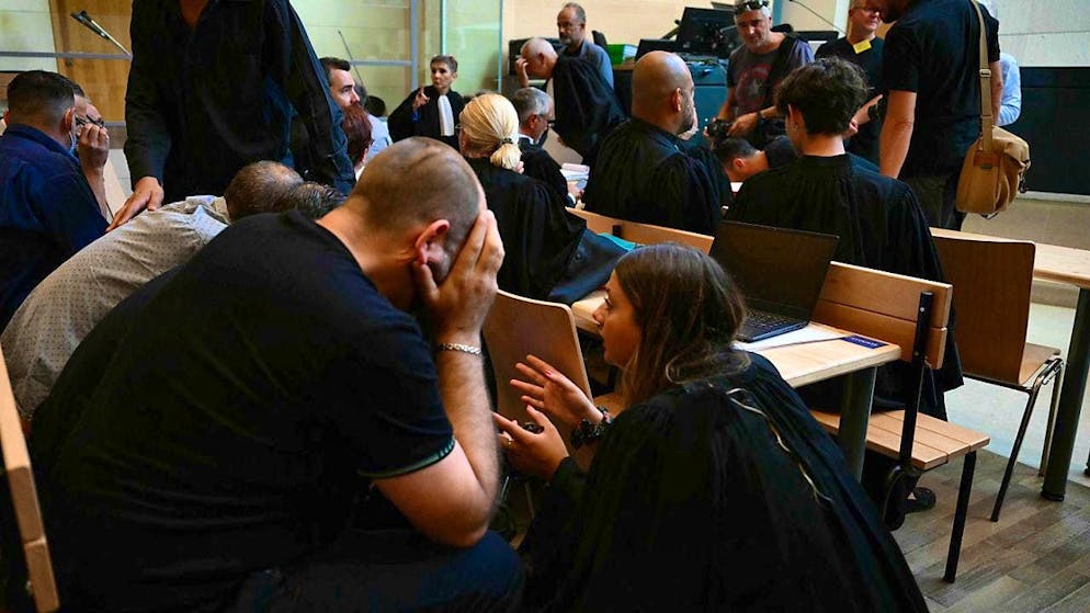 In front of the press and the victim's family: co-defendants speak with a lawyer in the courthouse.