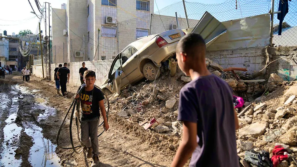 Palestinian refugees walk past a damaged vehicle in a refugee camp in the West Bank after an Israeli army military operation. Photo: Nasser Nasser/AP/dpa