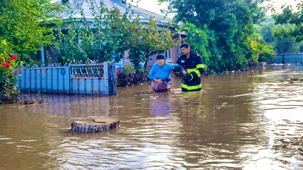 HANDOUT - In this photo, a rescuer helps a woman leave a house after torrential rains trapped many people in flooded areas. Photo: ISU Galati Romanian Emergency Services/AP/dpa - ATTENTION: For editorial use only and only with full attribution of the above credit