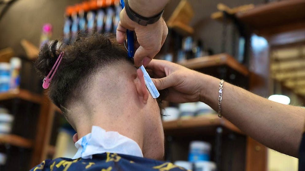 A hairdresser shaves the hair of a male customer in a barbershop. (symbolic image)