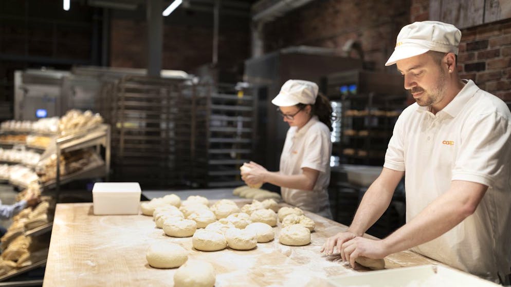In einer Coop-Filiale backen Mitarbeitende grosse und kleine Brötchen, die nach starken Regenfällen im Frühling und Sommer teurer werden. (Archivbild) 