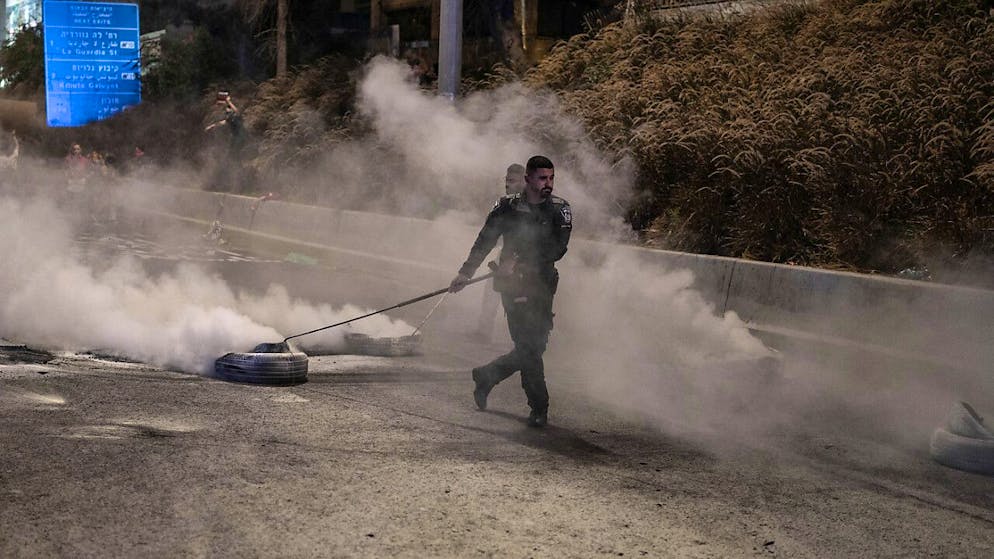 Ein israelischer Sicherheitsbeamter entfernt verbrannte Reifen von der Straße, nachdem die Familien und Unterstützer der von der Hamas entführten israelischen Geiseln versucht hatten, die Hauptstraße am jüdischen Feiertag Jom Kippur zu blockieren. Foto: Ilia Yefimovich/dpa