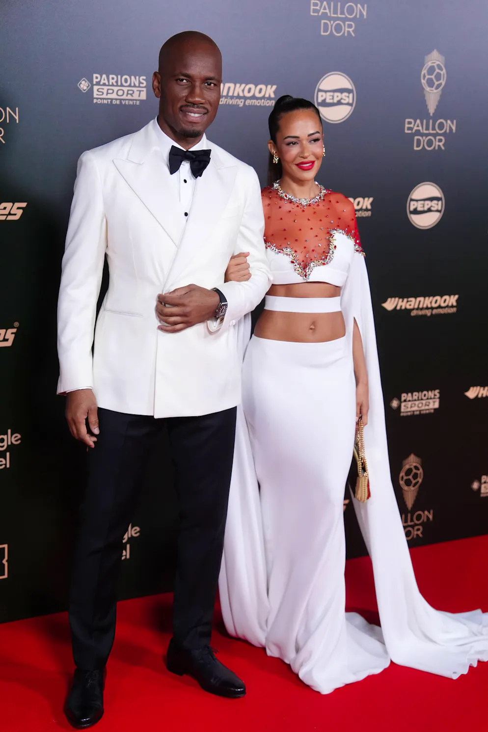 Ballon d'Or 2024. Didier Drogba dans un look noir et blanc et sa compagne Gabrielle Lemaire qui arborait une tenue à deux pièces avec un haut cropped et à manches extra-longues, mettant la mode libanaise à l'honneur.