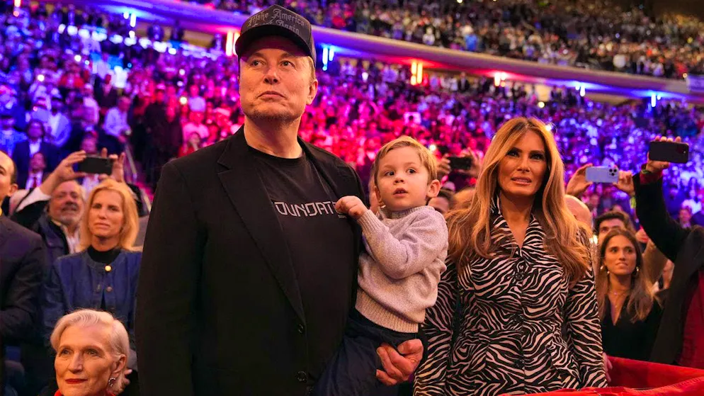 Elon Musk - with one of his eleven children in his arms - and Melania Trump (right) listen to Donald Trump at an election appearance in New York. (October 27, 2024)