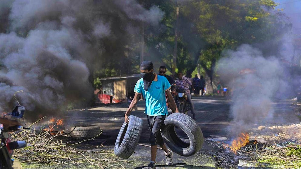 A resident carries tires to a burning barricade to keep gang members from entering his neighborhood in Port-au-Prince, Haiti.