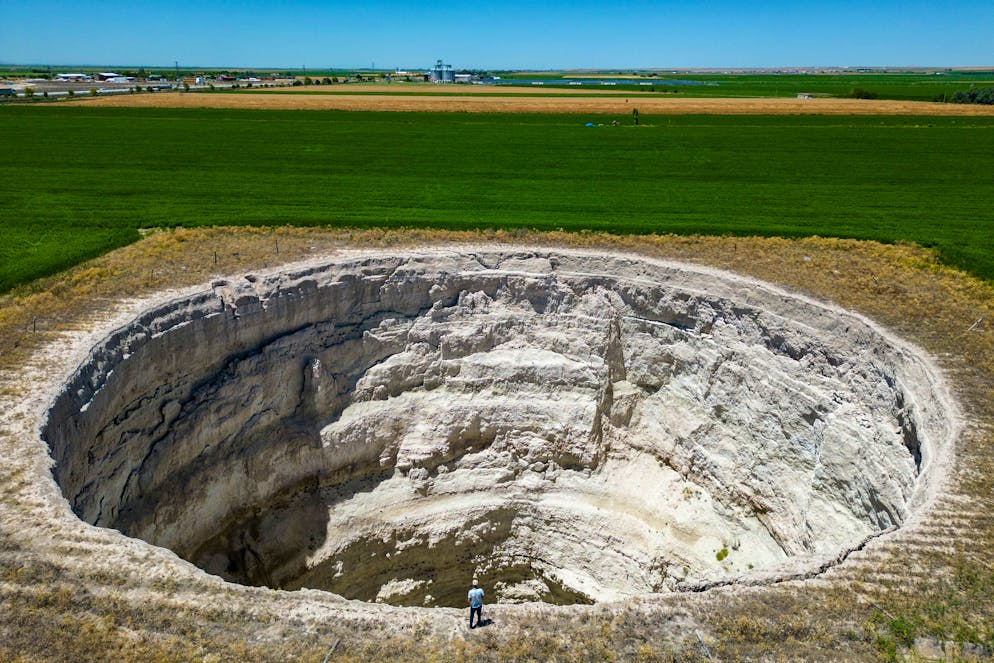 Cette photographie aérienne montre l'agriculteur Yigit Aksel marchant autour d'un gouffre géant formé au milieu des champs à Karapinar, dans la province de Konya en Anatolie centrale, le 23 juin 2024. - Les dolines existent depuis des siècles à Konya, une vaste province agricole connue pour être le grenier à blé de la Turquie, mais leur nombre a augmenté ces dernières années en raison de la sécheresse croissante et de la surutilisation des eaux souterraines pour l'irrigation, selon les experts. (Photo Yasin AKGUL / AFP)