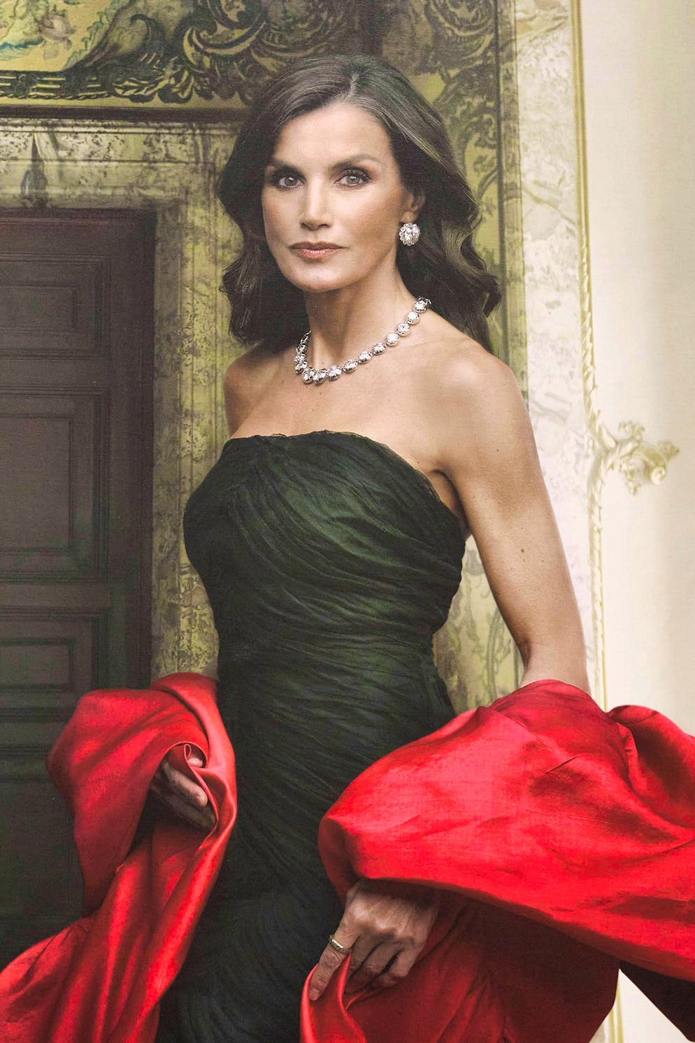 In the new portrait pictures, Queen Letizia wears a black, off-the-shoulder dress by Balenciaga, with a red silk scarf and diamond jewelry.