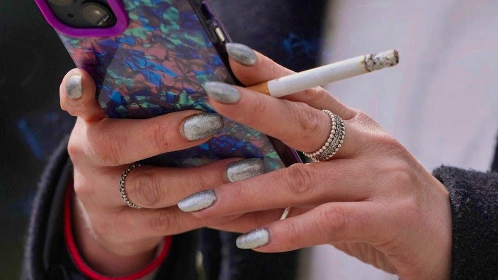 ARCHIVE - A woman smokes on a street while looking at her cell phone. Photo: Kin Cheung/AP/dpa