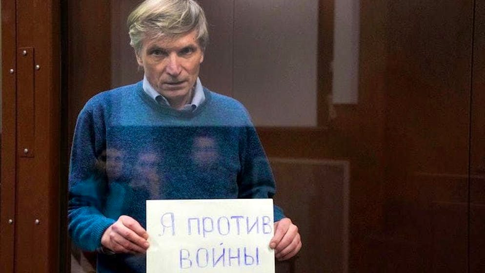 Alexei Gorinov holds a sign reading "I am against the war" in a cage during a courtroom hearing in Moscow.