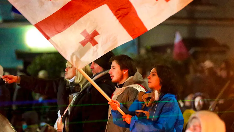 A demonstrator holds a Georgian national flag in front of the parliament building in front of the police. Photo: Zurab Tsertsvadze/AP/dpa